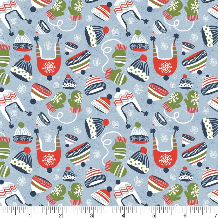 A repeating holiday-themed pattern on a light blue background featuring red, green, white, and navy knit hats, mittens, skates, snowflakes, and small white curved lines. A white ruler with black markings is visible along the bottom edge.